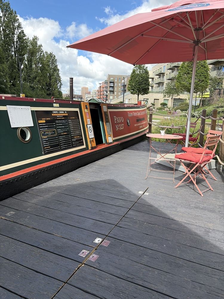 The boat's deck terrace with a red parasol and red bistro table and chairs beside the hull