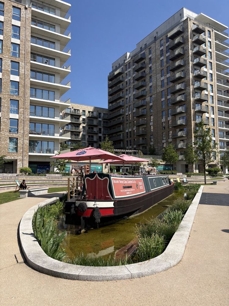The moored crepe narrowboat with its red parasol on the canal, apartment blocks behind