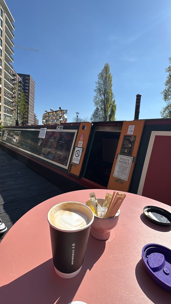 A takeaway latte on a pink outdoor table beside the boat under blue sky