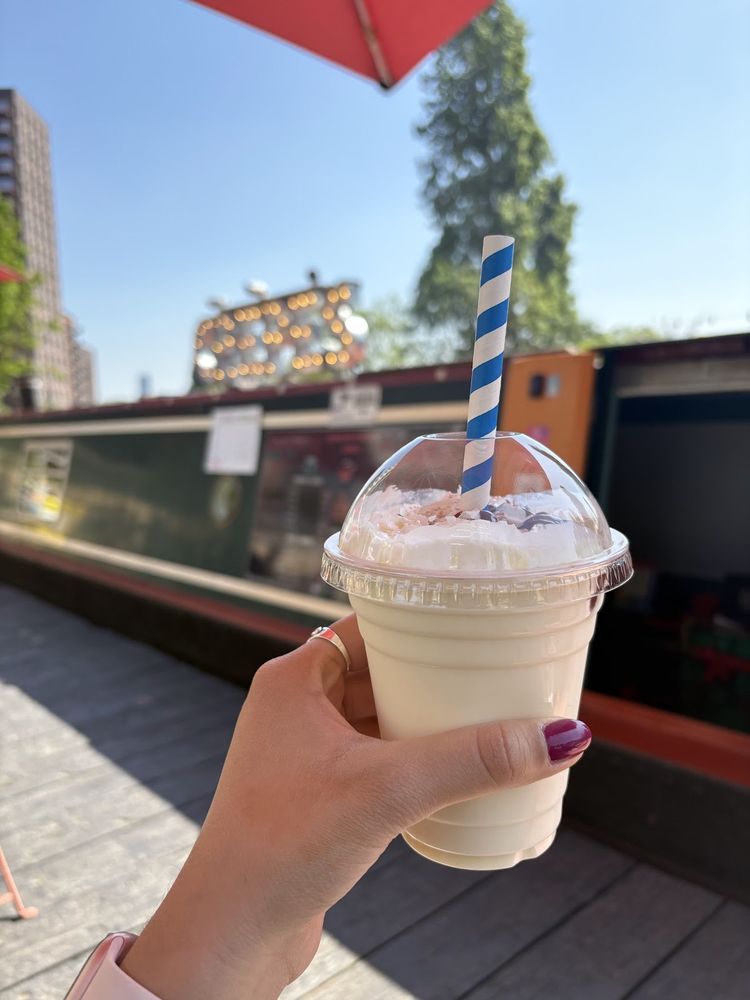 A hand holding a clear cup of a pale iced drink with a striped straw in front of the boat